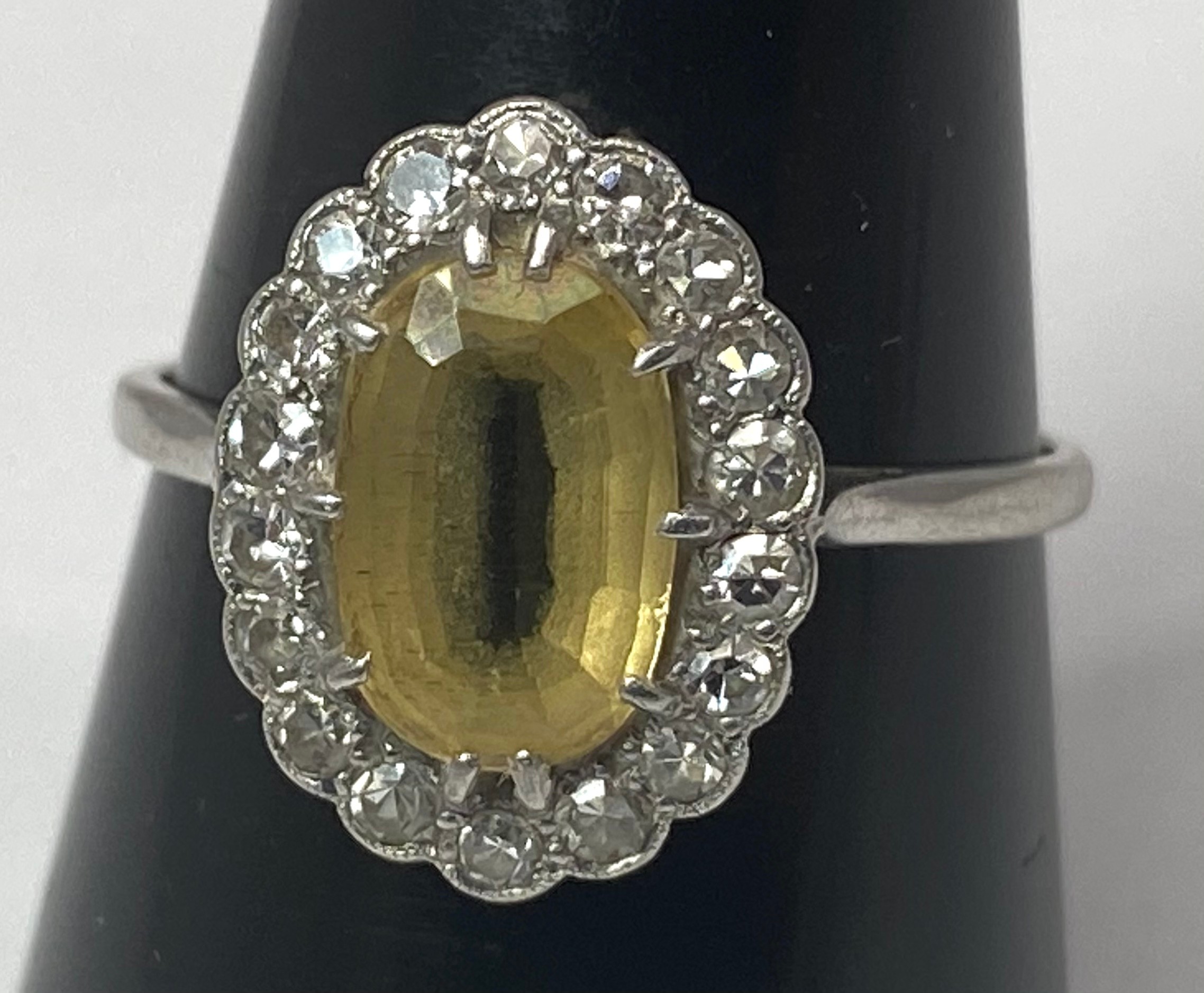 A platinum dress ring set with an oval citrine to the centre, surrounded by 18 x small diamonds in a