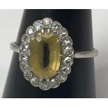 A platinum dress ring set with an oval citrine to the centre, surrounded by 18 x small diamonds in a