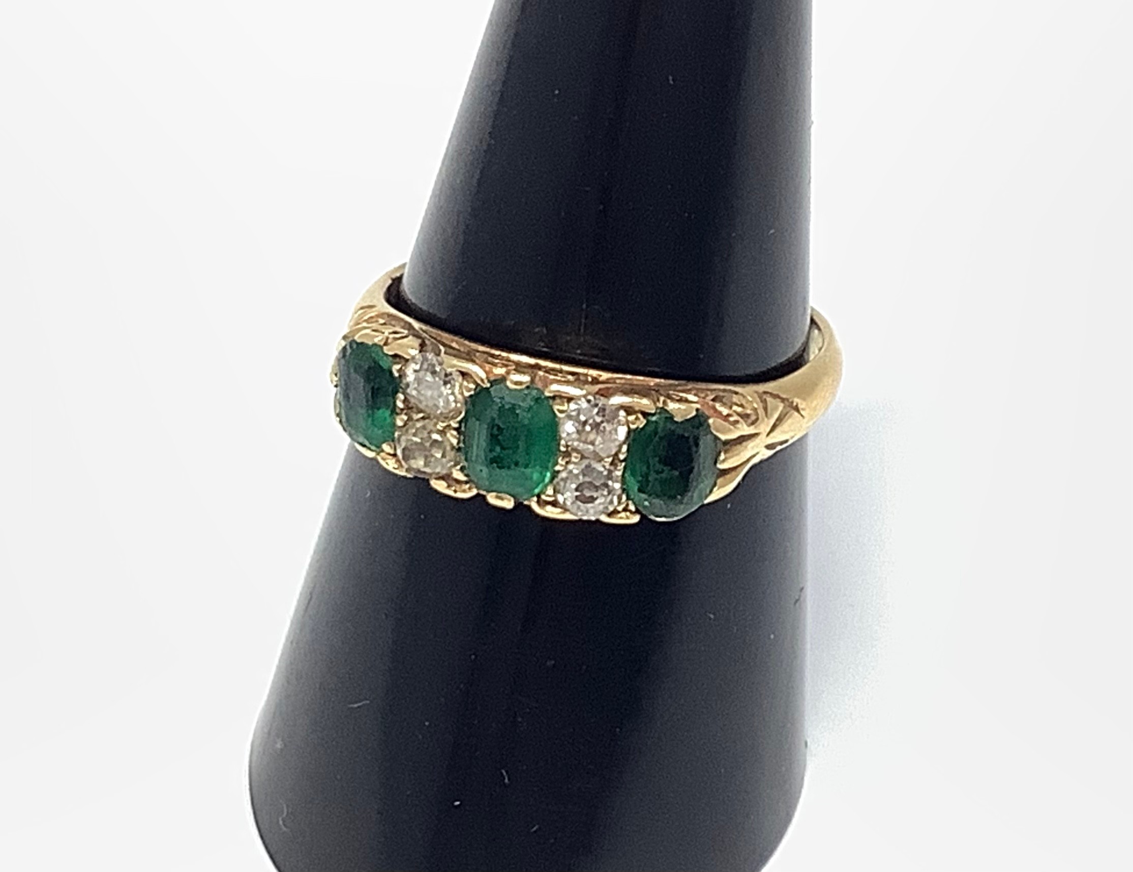 An 18ct gold ring set with three emerald coloured stones interspaced by two pairs of diamonds, 3.8g,