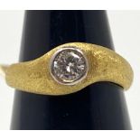 An 18ct yellow gold textured design solitaire diamond ring, the round brilliant cut diamond in a