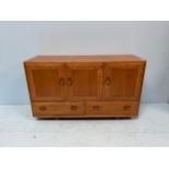 An Ercol Blonde elm Windsor sideboard, with three cupboard doors enclosing shelves, above two