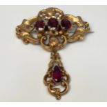 A 9ct gold pierced oval shaped brooch with pendant drop, set with garnet coloured stones, 7 x 5.5cm,