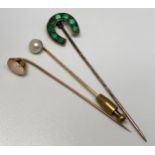 Three various yellow metal tie pins including a horseshoe set with green coloured stones, one with