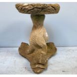 A low stone bird table, the circular top raised on three stylised dolphin supports, 44cm tall