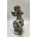 A cast iron garden statue of a cherub sat on a ball with hands covering eyes and crossed legs,