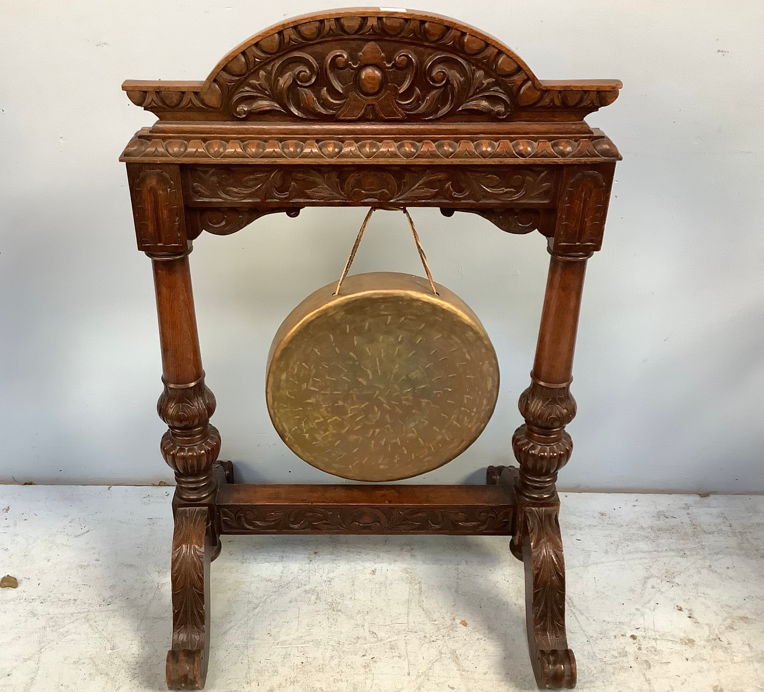 A carved oak framed floor-standing dinner gong, with foliate carved arched top, raised on scrolled