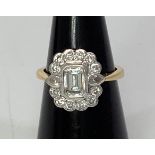 An 18ct yellow gold and diamond cluster ring, centrally bezel set an emerald-cut diamond,