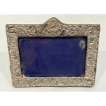 A silver easel picture frame of rectangular form, with scrolled and floral decoration, with glass,
