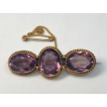 A yellow metal (tests as 14 or 15ct) brooch set with three oval faceted amethyst coloured stones