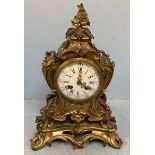 A French gilt bronze mantel clock with floral cast finial, scrolled sides, white enamel dial with