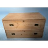 A stripped pine campaign style chest of two drawers with flush brass handles and twin carry-handles,