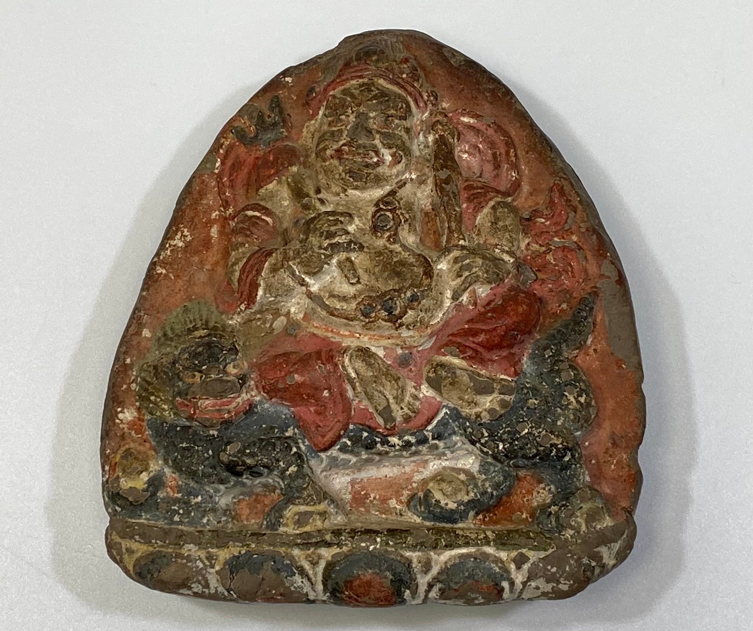 A 19th century Tibetan clay amulet painted with a Buddhist deity, possibly Vaishravana, riding a foo