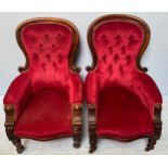 A pair of Victorian walnut armchairs with button-back deep red upholstery, raised on turned supports