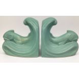 A pair of green-glazed Langley Pottery bookends modelled as dolphins on wave crests, designed by