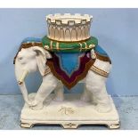 A large porcelain figure of an elephant carrying a howdah on a green tasselled cushion and purple,