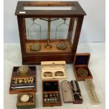 A large set of balance scales in wooden glazed display case, retailer’s plaque ‘Griffin, Sardinia