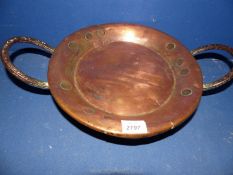 A copper two handled, three legged bowl.