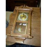 A light wood wall clock with pendulum by Daniel Dakota. 23" long.