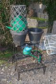 A three tier plant stand, hose pipe, watering can and planters.