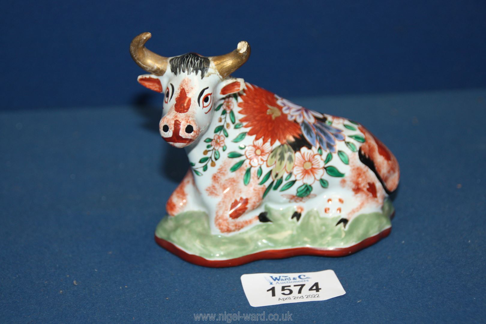 An antique Delft pottery figurine of a seated cow decorated in polychrome; (damage to one horn),