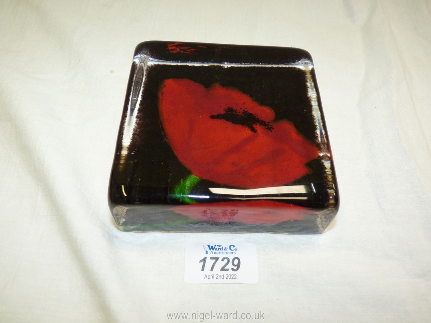 A heavy Caithness square 'Sandcast Glass' paperweight with Poppy resting on dark ground.