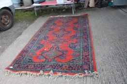 A bordered, patterned and fringed Rug in red, blue and green with five medallions to the centre,