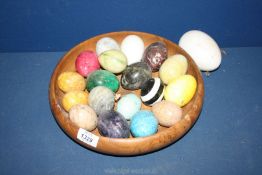 A quantity of marble and onyx eggs in wooden bowl.