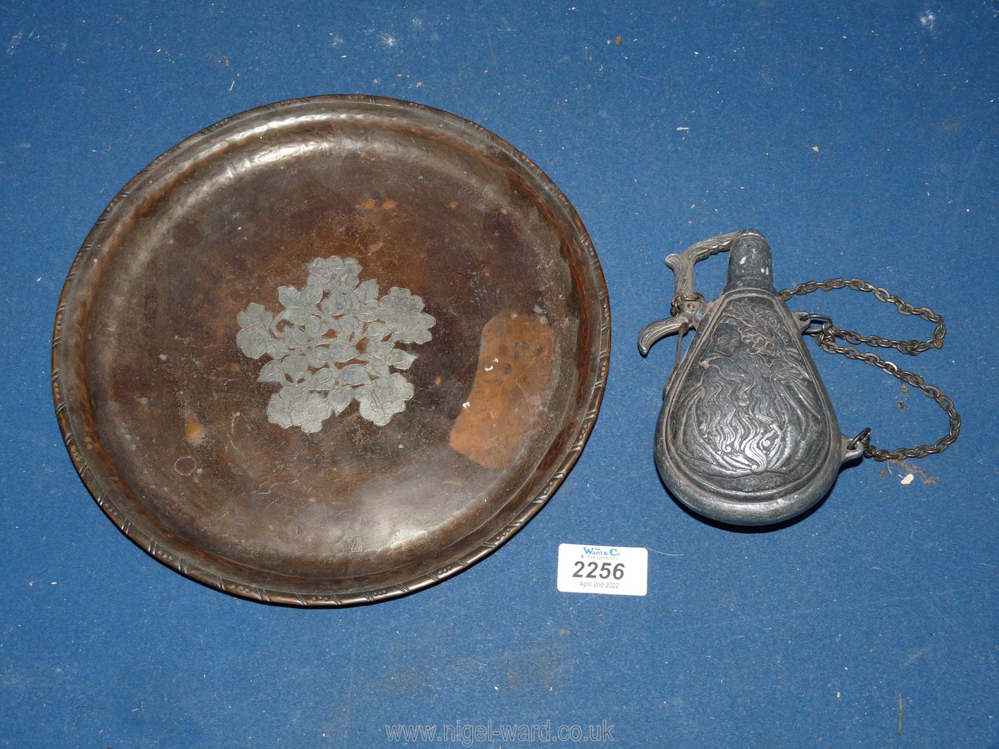 An embossed copper plate and a pewter gun powder flask.