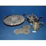 A heavily embossed white metal fruit basket with handle, a teapot and coasters.