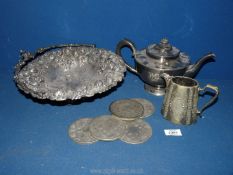 A heavily embossed white metal fruit basket with handle, a teapot and coasters.