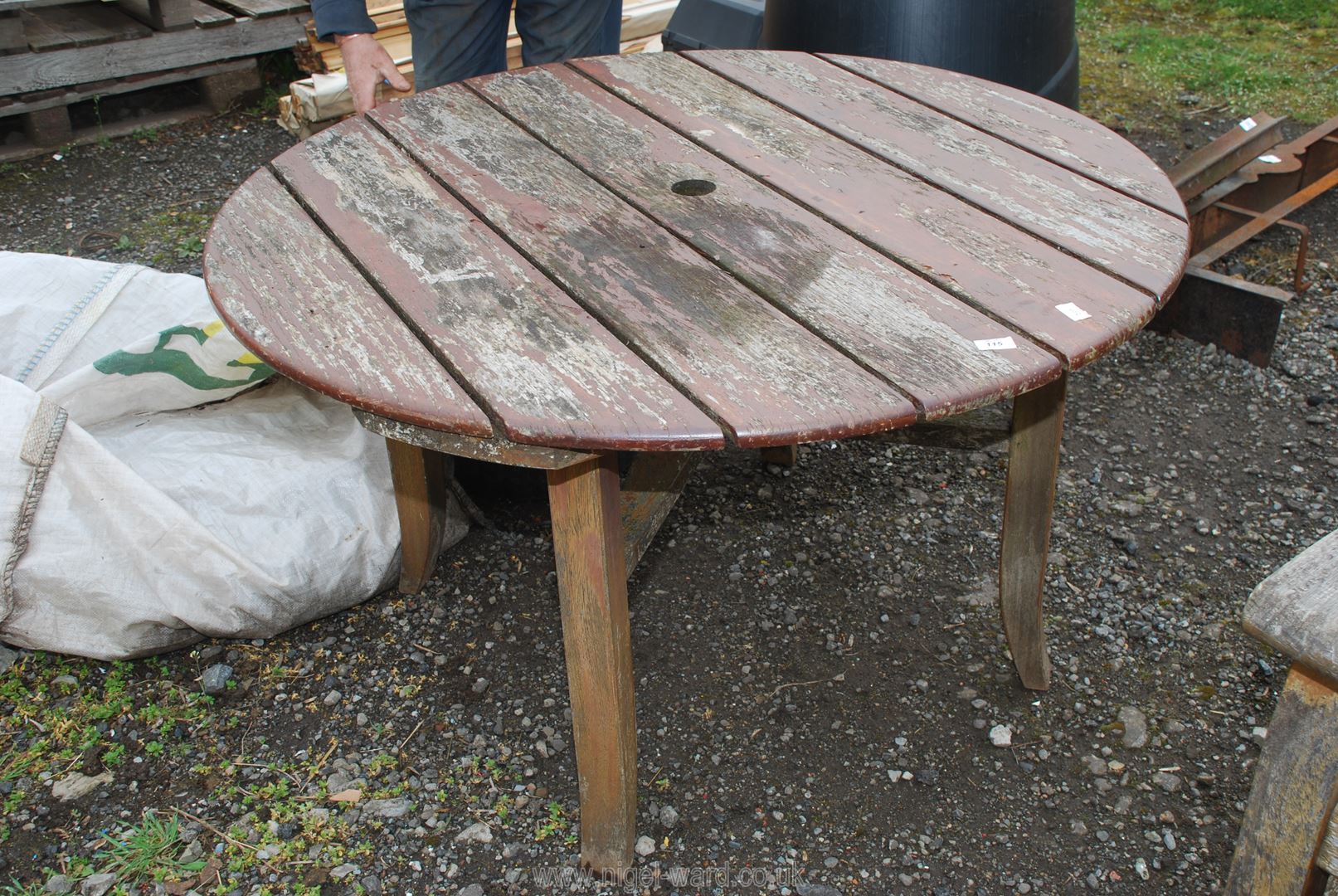 A circular garden table on four legs with space for parasol, 47'' diameter.