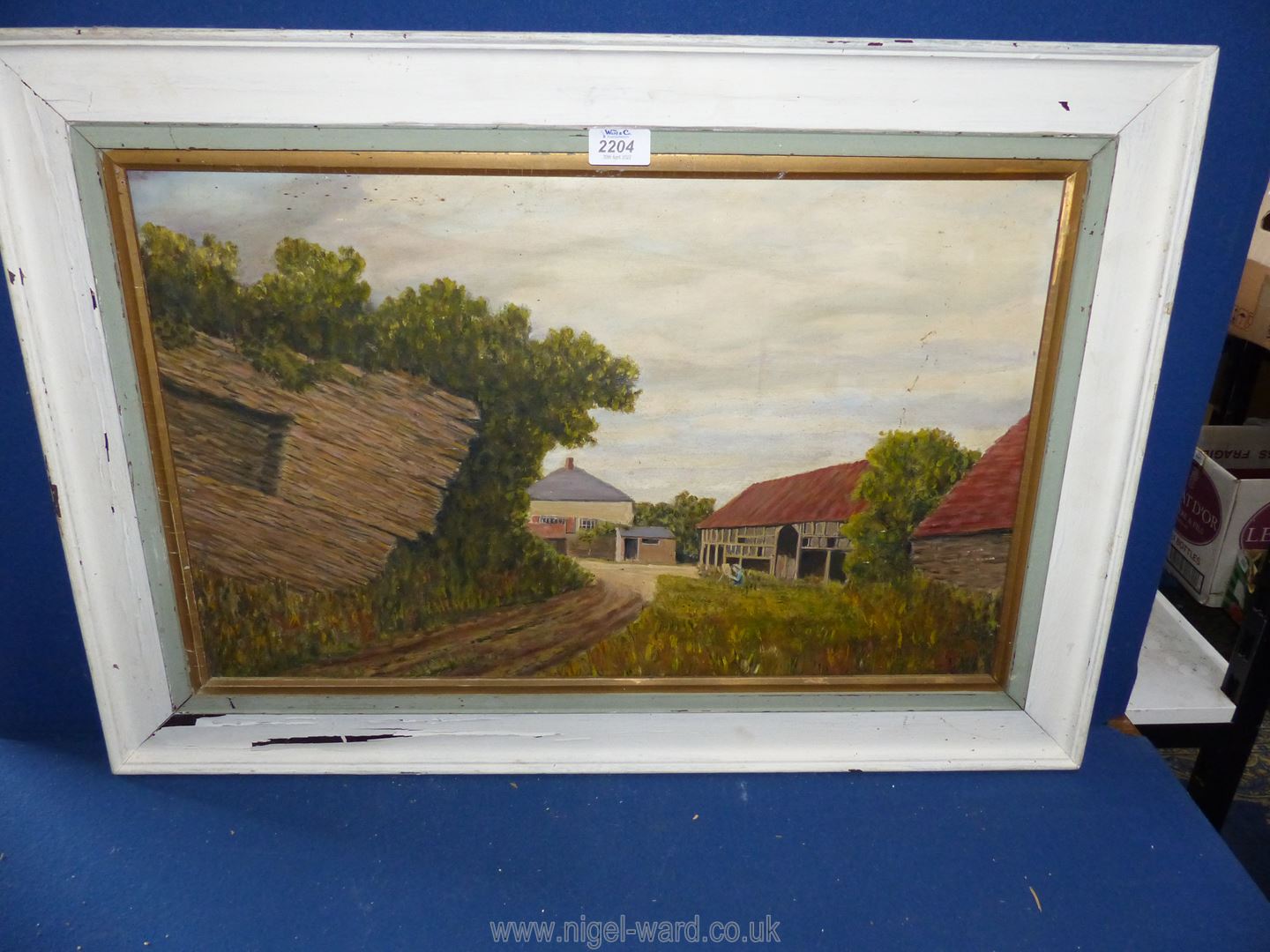 A wooden framed Oil on board depicting a farmyard with old barns and an artist sat amongst the