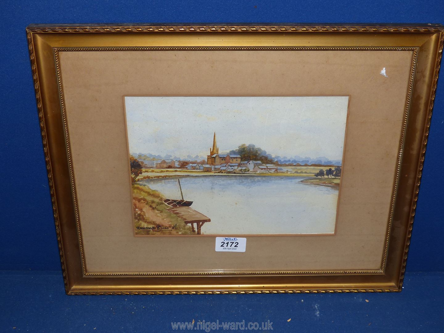 A framed and mounted Watercolour depicting a River landscape with village in the distance,