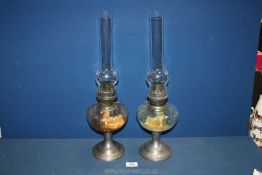 A pair of Pewter Oil Lamps with glass reservoirs and clear glass chimneys, 19 1/2'' tall.