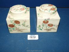 A pair of Ivory shaded square shaped caddies with one interior lid missing under the covers and