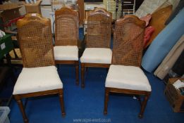 A set of four rattan backed dining chairs with cream fabric seats