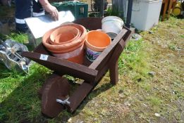 A small wooden wheelbarrow containing terracotta pots.