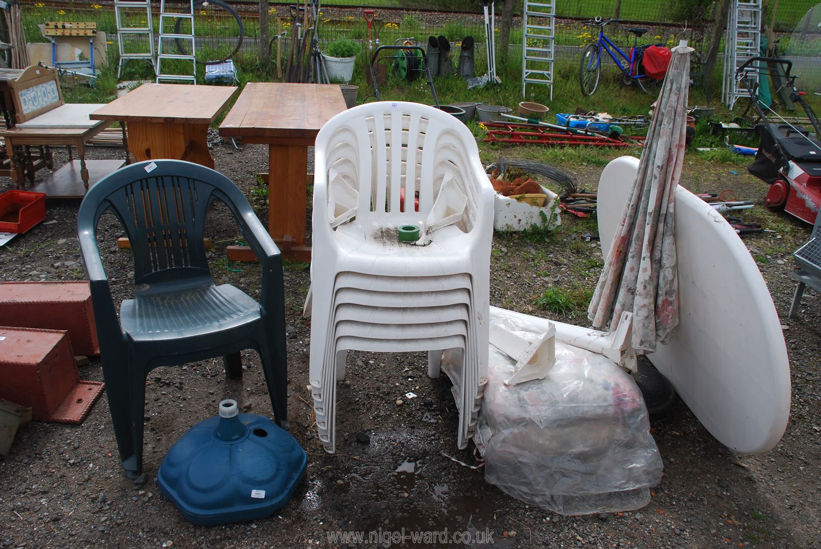 Five white plastic chairs and white oval patio table with umbrella and stand, plus two green chairs.