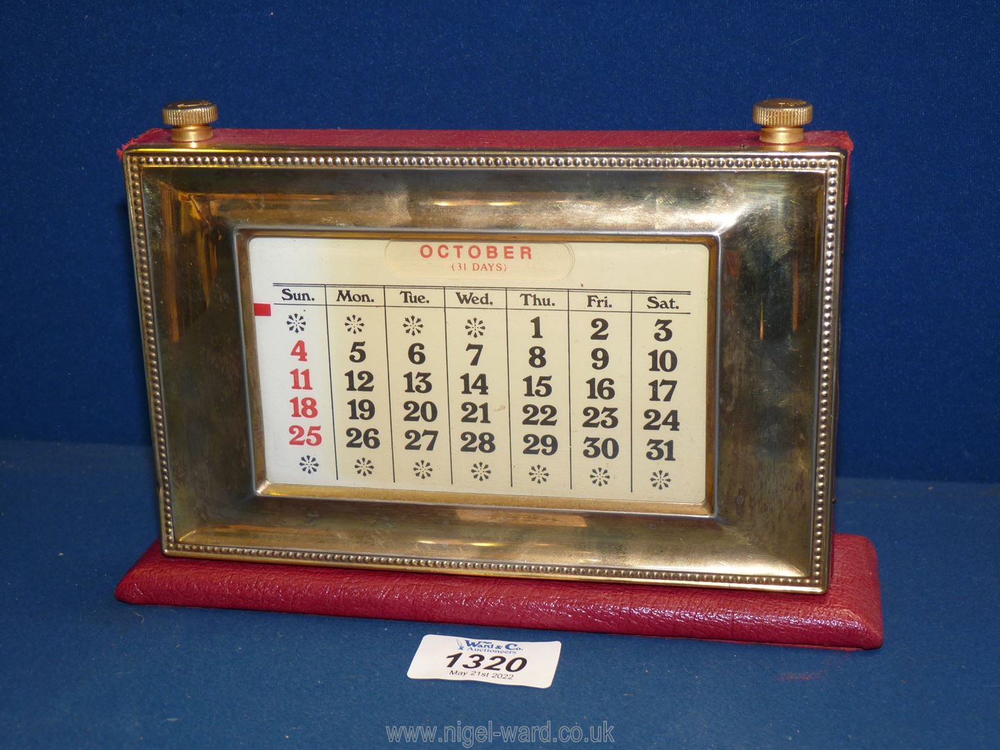 A brass fronted perpetual Calendar on red leather base, 8 1/4'' at base x 5 1/2'' tall.