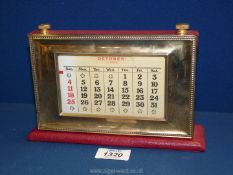 A brass fronted perpetual Calendar on red leather base, 8 1/4'' at base x 5 1/2'' tall.