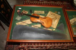 A Violin in large display case including bow, no strings, music sheets and violin parts displayed,