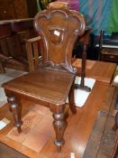 A solid seated mixed hardwoods Hall Chair having a shaped back with heraldic shield and standing on