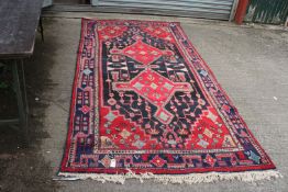 A large Iranian rug, red/navy and black with border pattern and fringing to one end,