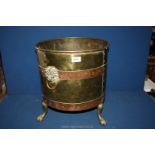 A large brass coal bin on three claw feet with lion head handles on both sides,