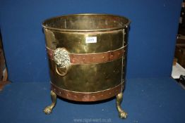 A large brass coal bin on three claw feet with lion head handles on both sides,