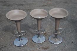 Three retro bar stools on chrome bases by Magis with beige coloured seat.
