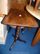 A small Walnut topped occasional table standing on turned pedestal on pirouette feet,