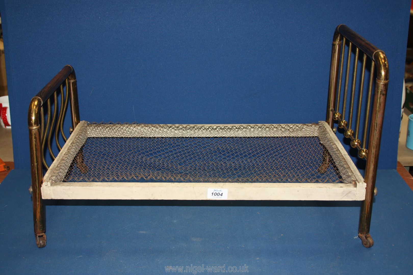 A Victorian dolls bed with brass ends, wooden frame and wire mesh base,