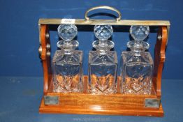 A Tantalus with three square cut glass decanters and white metal handle and corners,