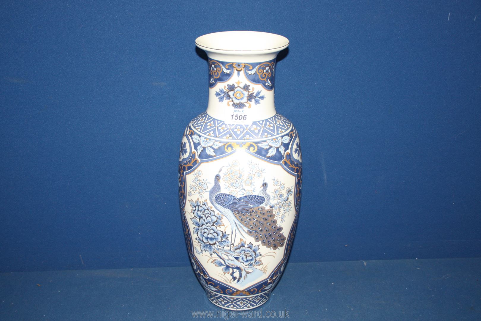 An oriental style Vase with panels of blue and gold Peacocks between floral detail on a white